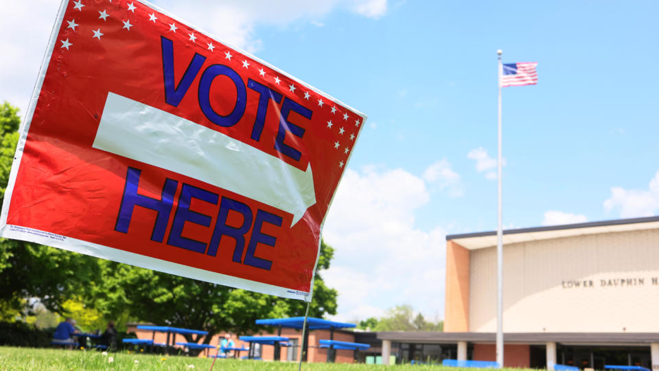 A red sign with a white arrow and blue lettering, which reads: Vote here.