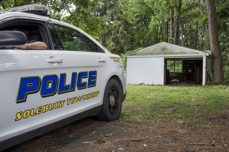 A Solebury Township policeman guards a garage on Aquetong Road where investigators found the car of one of the four missing men. (CLEM MURRAY / Staff Photographer)