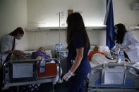 In this Thursday, May 7, 2020 photo, medical students Afroditi Gerodimontaki, left, Michaella Alexandrou, center, and Dimitra Siakalli examining patients patients at the Pathological Clinic of Sotiria Hospital in Athens. Greece's main hospital for the treatment of COVID-19 is also the focus of a hands-on training program for dozens of medical students who volunteered to relieve hard-pressed doctors from their simpler duties while gaining a close peek at the front lines of a struggle unmatched in modern medical history. (AP Photo/Thanassis Stavrakis)