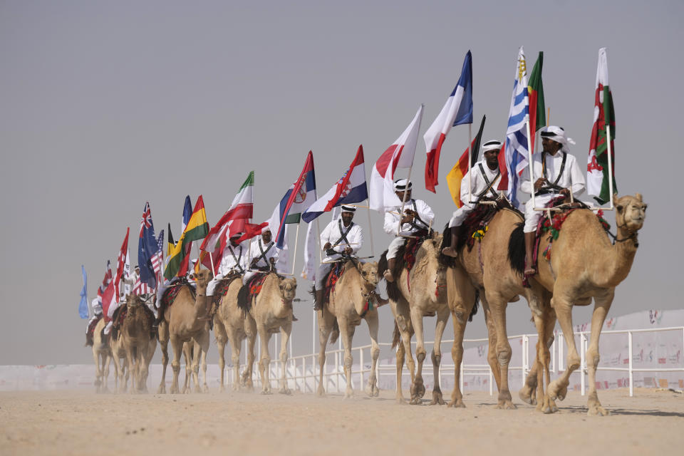 Camel parade with flags during a pageant at the Qatar camel Mzayen Club, in Ash- Shahaniyah, Qatar, Friday, Dec. 2, 2022. (AP Photo/Alessandra Tarantino)