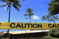 With beachgoers in the background, yellow caution tape is wrapped across an area of Waikiki, Friday, March 20, 2020, in Honolulu. Honolulu closed all public parks and recreation areas Friday until the end of April in an effort to help stop the spread of the coronavirus. (AP Photo/Marco Garcia)