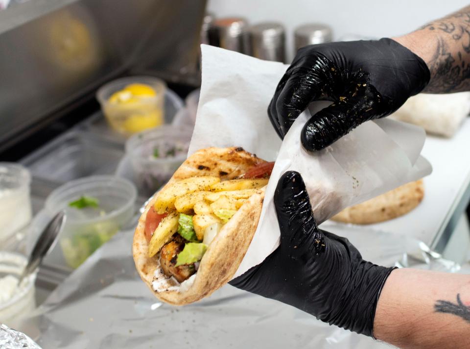 Locals Gon Greek food truck owner Evangelos Varonos creates one of his Greek-inspired wraps as he completes a customer's order on Tuesday, April 11, 2023. 