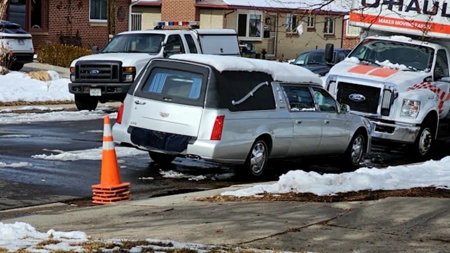 A silver hearse parked on a residential street with homes