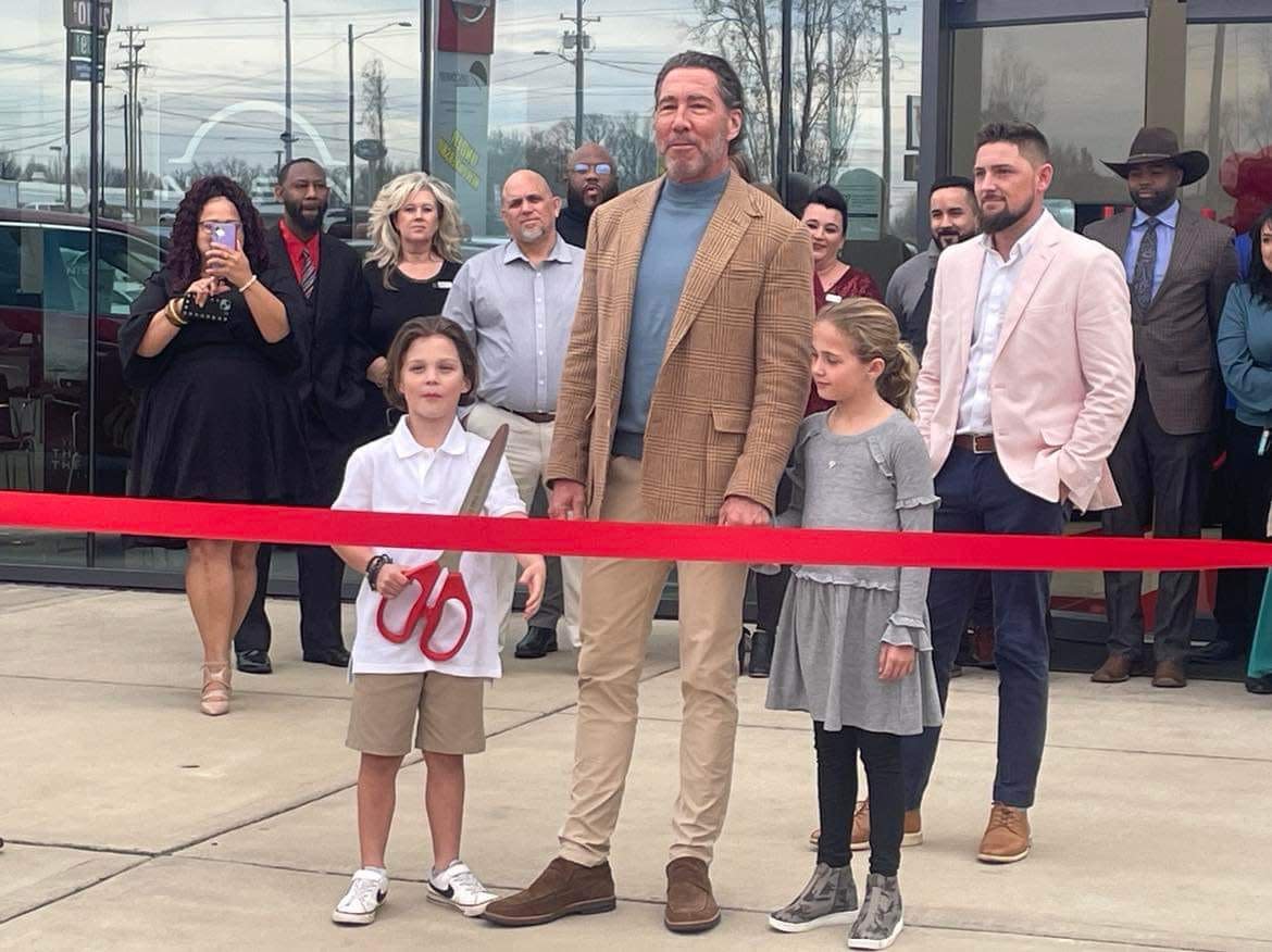 Kevin Geagan, new owner of Discovery Nissan, cuts the ribbon with his children at the grand opening of the dealership held last week.