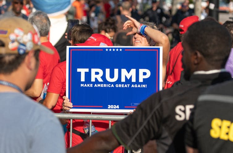 A person holds a 'Trump – Make America Great Again' sign up at a rally.