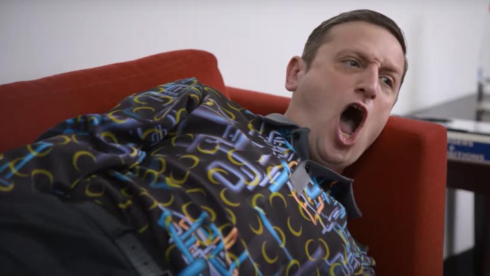 A man in a patterned shirt lies down on a red couch screaming