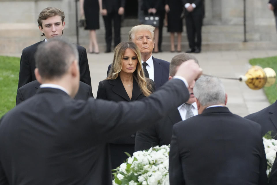 Former President Donald Trump stands behind his wife Melania as she watches a priest wave incense around the coffin of her late mother Amalija Knavs, Thursday, Jan. 18, 2024, at the Church of Bethesda-by-the-Sea in Palm Beach, Fla. Standing at rear left is their son Barron. (AP Photo/Rebecca Blackwell)