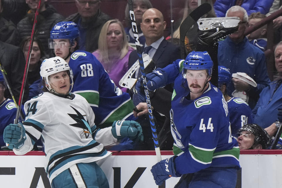 Linesman Scott Cherrey, back right, falls into the Vancouver bench after San Jose Sharks' Alexander Barabanov (94) and Vancouver Canucks' Kyle Burroughs (44) collided during the third period of an NHL hockey game in Vancouver, British Columbia, Thursday, March 23, 2023. (Darryl Dyck/The Canadian Press via AP)