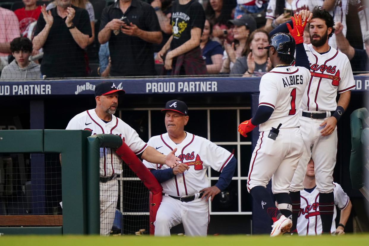 Atlanta Braves' Ozzie Albies (1) is greeted at the dugout by coach Walt Weiss, left, manager Brian Snitker and shortstop Dansby Swanson after hitting a home run during the first inning of the team's baseball game against the Florida Marlins on Saturday, April 23, 2022, in Atlanta. (AP Photo/John Bazemore)
