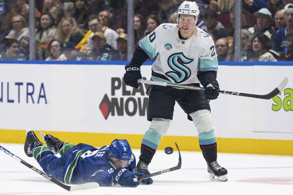 Vancouver Canucks' Conor Garland (8) passes the puck while he falls, as Seattle Kraken's Eeli Tolvanen (20) watches during the second period of an NHL hockey game Saturday, Nov. 18, 2023, in Vancouver, British Columbia. (Ethan Cairns/The Canadian Press via AP)