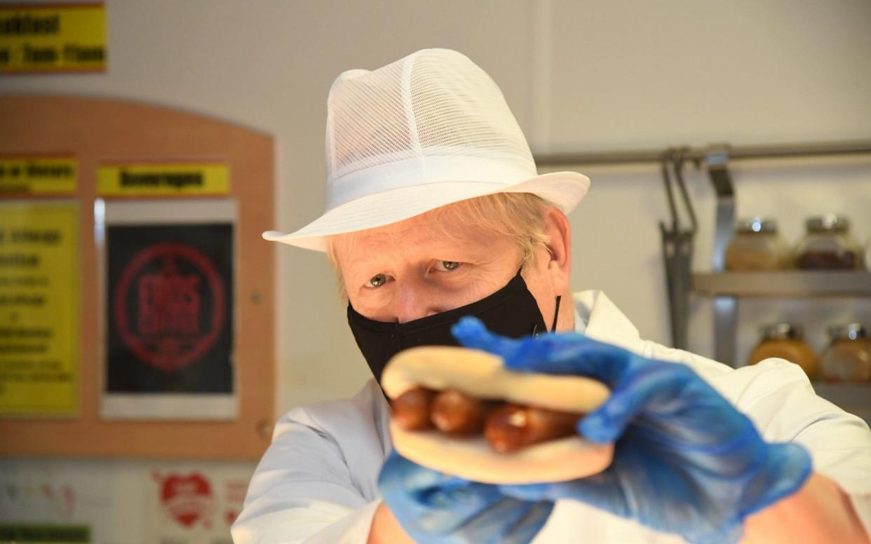 Prime Minister Boris Johnson holds up a sausage filled roll as he assists kitchen staff during a visit to Royal Berkshire Hospital - Jeremy Selwyn//PA