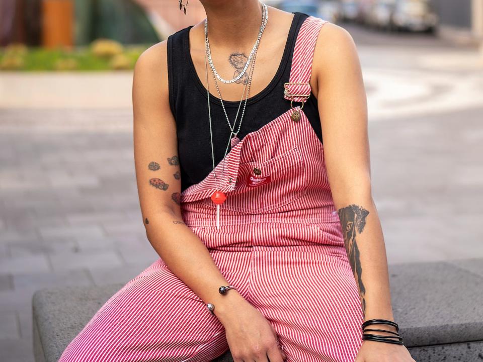 person wearing a black tank top and striped overalls on a concrete bench