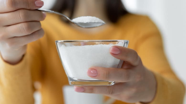 Hands holding a spoon and dish full of white sugar