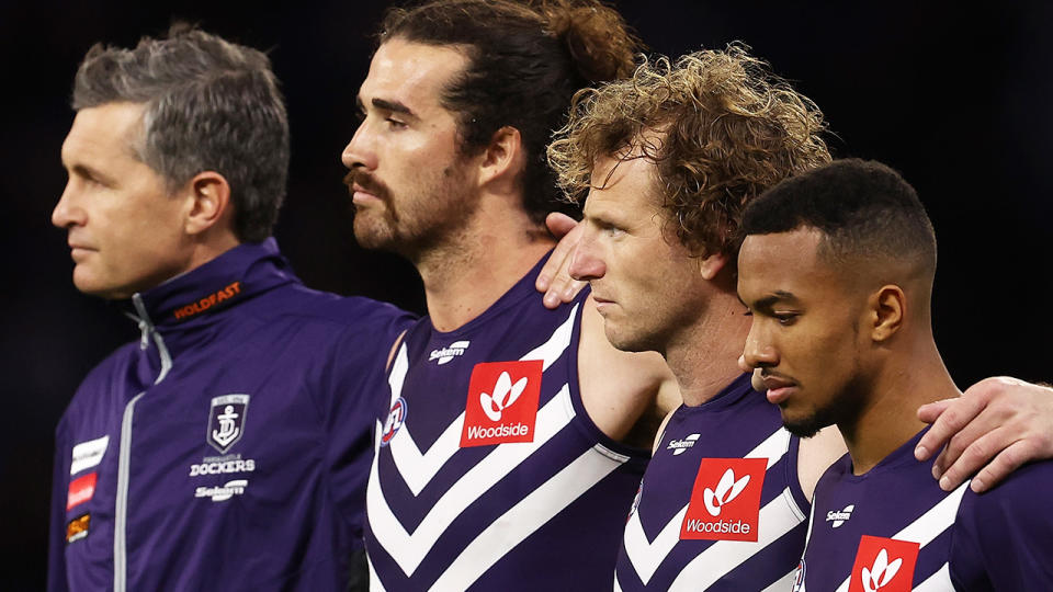 Fremantle Dockers players are seen lined up for the Australian anthem, with guernseys featuring a prominent red Woodside logo.