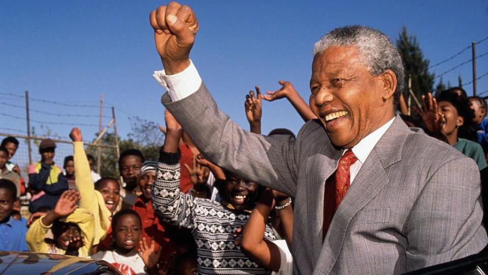 Nelson Mandela raising his fist in the air amongst a group of young South Africans