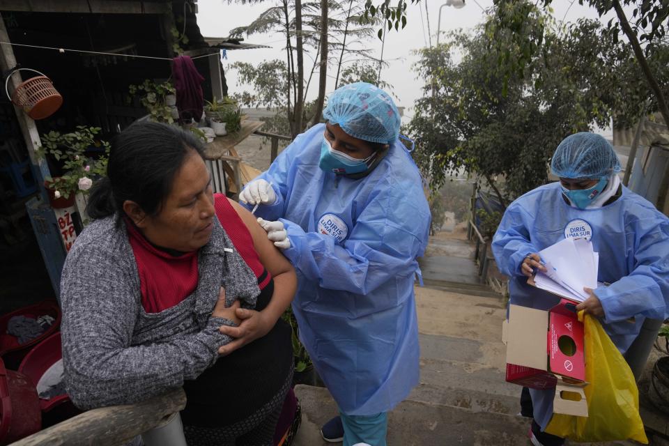Marlith Fasabi recibe la dosis de la vacuna contra la gripe y la vacuna Moderna contra el COVID-19 durante una campaña de vacunación puerta a puerta en el barrio Ticlio Chico en las afueras de Lima, Perú, en el primer día oficial de invierno, el martes 21 de junio de 2022. (Foto AP/Martín Mejía)