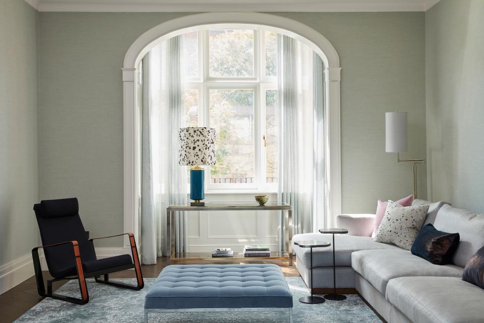 This relaxing family room features side tables by Tom Faulkner, an ottoman by Knoll, and an armchair by Vitra. Table lamp is by Nicholas Haslam while the floor lamp is from Visual Comfort. The walls are covered with sea green linen by Phillip Jeffries.