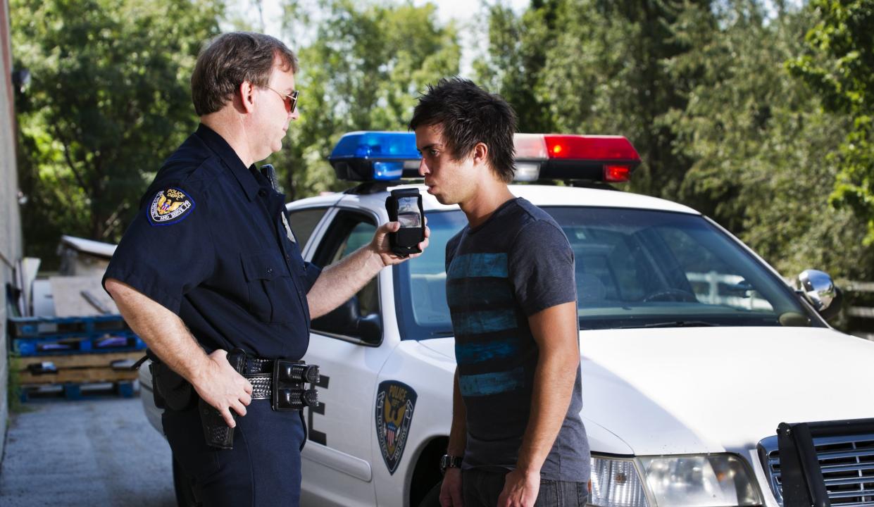 Stock photo of a police officer standing by his car giving a young man a breathalizer test.