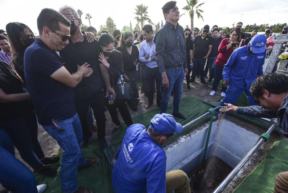 Mortuary workers lower a coffin into a grave as mourners look on