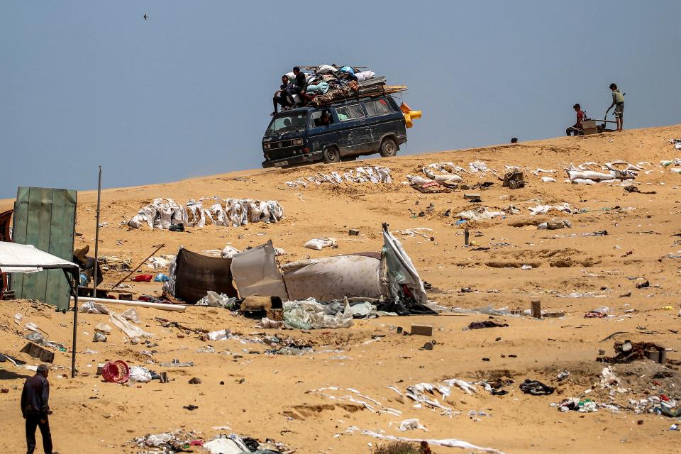 Two men ride atop a minibus loaded with mattresses, covers and other items as they return to Khan Younis in the southern Gaza Strip on May 14, 2024.