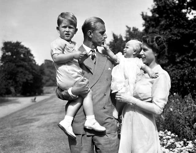 Princess Anne in the arms of Princess Elizabeth, with the Duke of Edinburgh, holding Prince Charles, in the grounds of Clarence House, their London residence