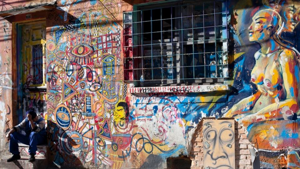 A man sitting with his head in his hands in front of a wall with street art grafitti on it, Vila Madalena neighbourhood, Sao Paulo, Brazil. (photo by Phil Clarke HIll/In Pictures via Getty Images)