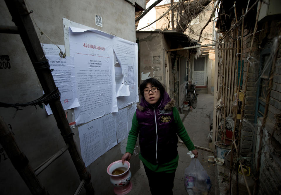 In this photo taken on Dec. 26, 2012, a Chinese woman walks out from her Hutong home with a demolition notice seen on the wall near the historical Drum and Bell Tower in Beijing. The district government wants to demolish these dwellings, move their occupants to bigger apartments farther from the city center and redevelop a square in 18th century Qing Dynasty fashion. (AP Photo/Andy Wong)