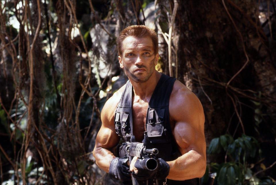 Arnold Schwarzenegger holds a massive gun in a jungle