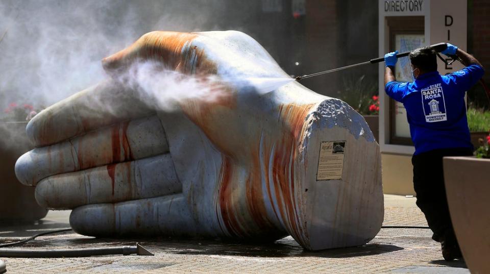 In this early Saturday morning, April 17, 2021, photo, a Santa Rosa downtown district maintenance worker cleans the "Agraria" hand sculpture vandalized with what appeared to be blood outside the Santa Rosa Plaza in Santa Rosa, Calif.