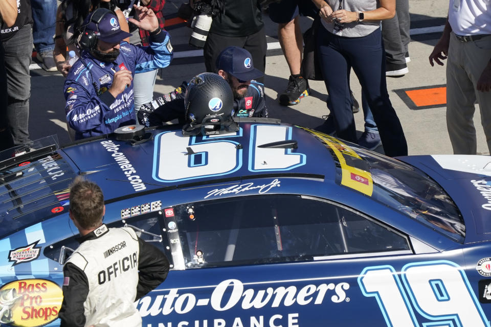 Martin Truex Jr., center, climbs into his race car before a NASCAR Cup Series auto race at Martinsville Speedway in Martinsville, Va., Sunday, Oct. 29, 2023. (AP Photo/Chuck Burton)