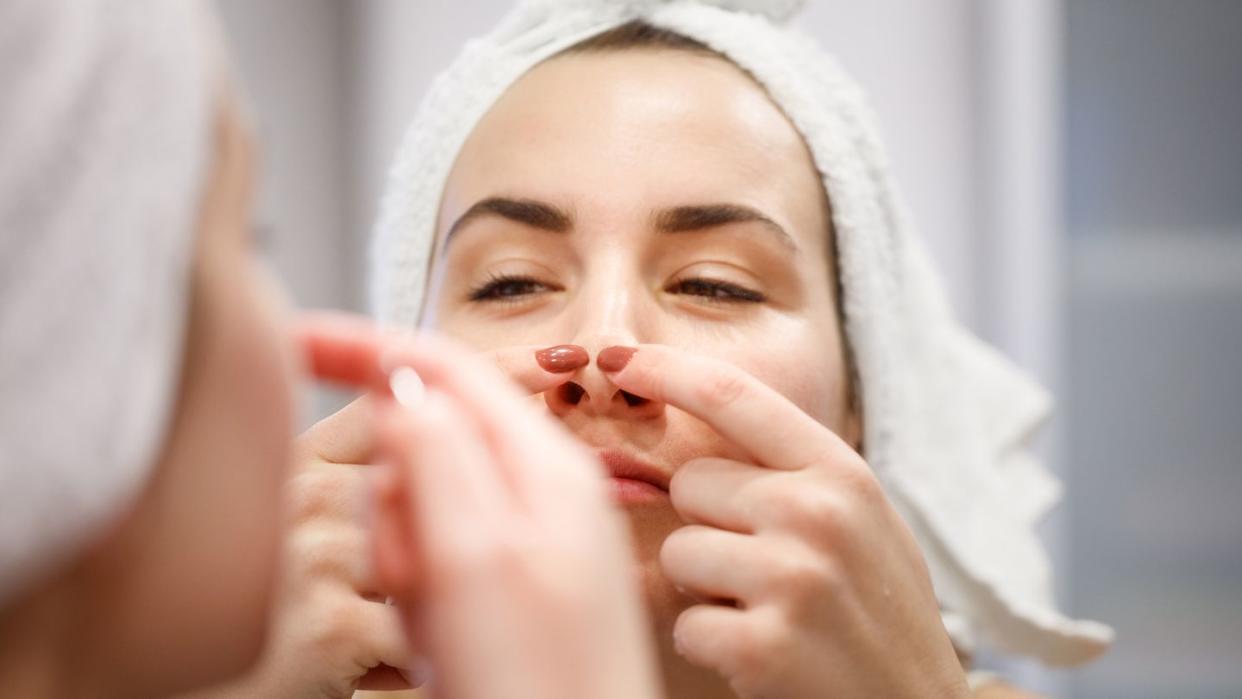 reflection of woman with towel on head squeezing blackhead on her nose