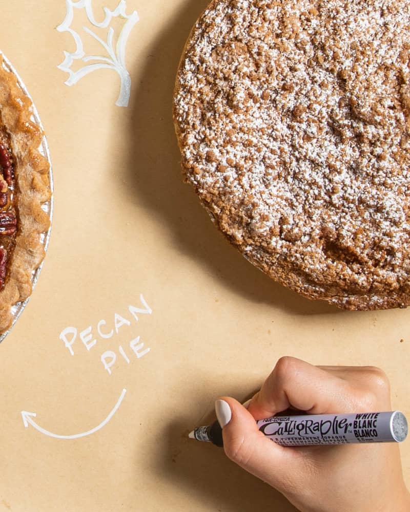 Overhead view of 2 pies and someone writing on craft paper with marker