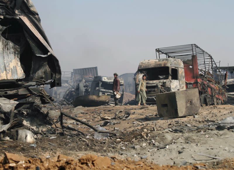 Men walk amidst wreckage of gas tankers after a fire in Islam Qala