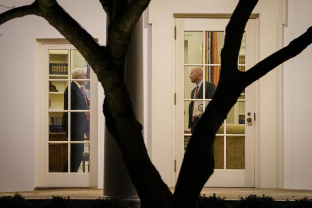 Seen through French windows behind a tree, Vice President Mike Pence talks to Marc Short, who is carrying a file of official papers.