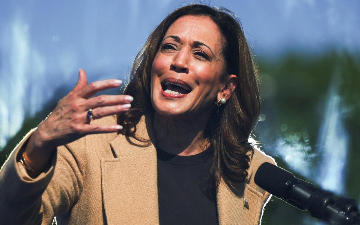 Ms Harris is seen gesturing at a lectern, through protective glass