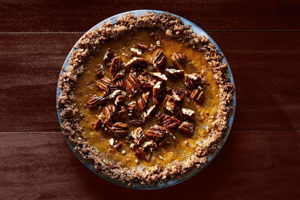 pumpkin pie with oat pecan crust in a metal pie plate with chopped pecans on top