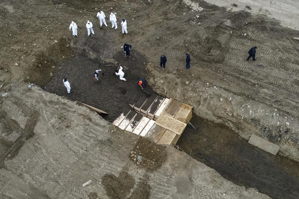 Workers wearing personal protective equipment bury bodies in a trench on Hart Island, Thursday, April 9, 2020, in the Bronx borough of New York. On Thursday, New York City’s medical examiner confirmed that the city has shortened the amount of time it will hold on to remains to 14 days from 30 days before they will be transferred for temporary internment at a City Cemetery. Earlier in the week, Mayor Bill DeBlasio said that officials have explored the possibility of temporary burials on Hart Island, a strip of land in Long Island Sound that has long served as the city’s potter’s field. (AP Photo/John Minchillo)