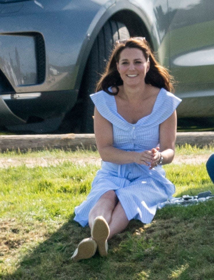 Kate Middleton sits on the grass and watches Prince William play polo.