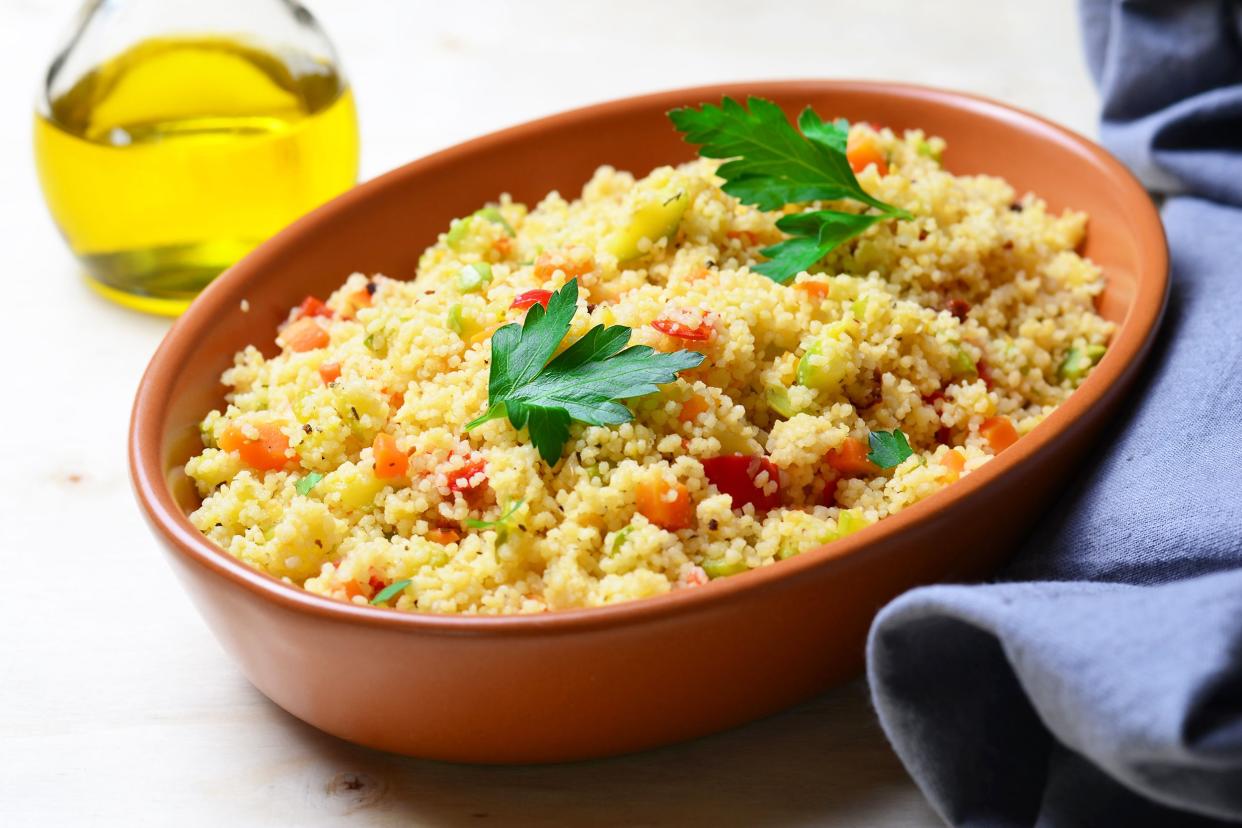 Couscous in a terracotta dish bowl with a blue napkin on the right on a white wooden table with oil olive in the background