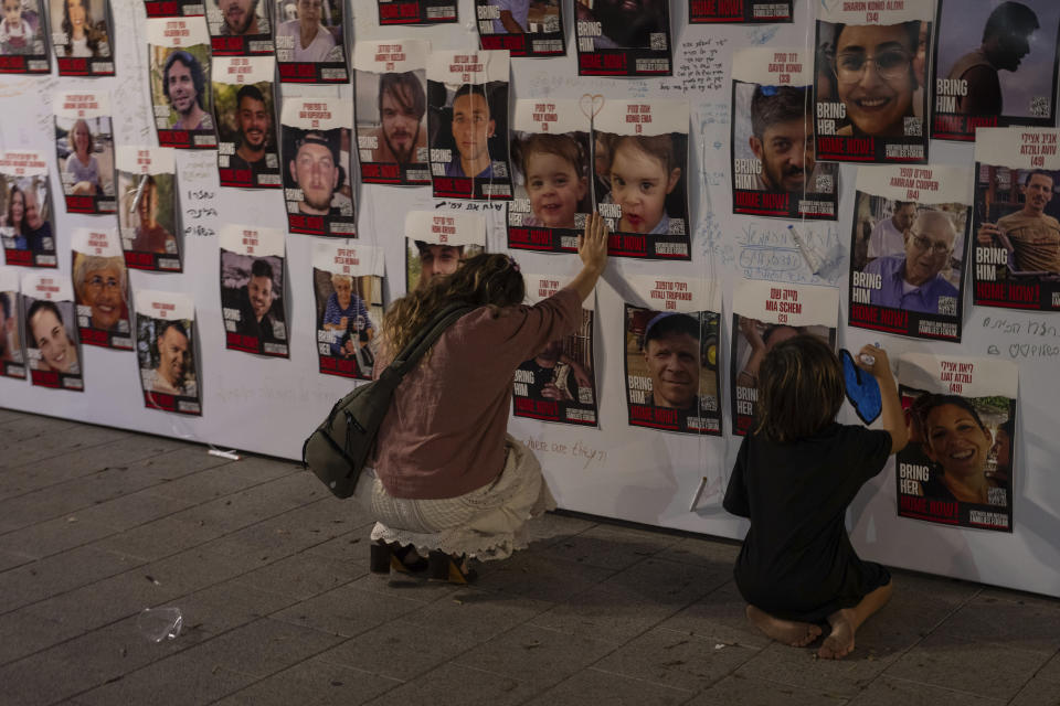 An Israeli woman touches photos of Israelis missing and held captive in Gaza, displayed on a wall in Tel Aviv, on Saturday, Oct. 21, 2023. Relatives of people kidnapped by Hamas militants and supporters organized a protest Saturday calling for the return of more than 200 hostages held in Gaza for two weeks. (AP Photo/Petros Giannakouris)
