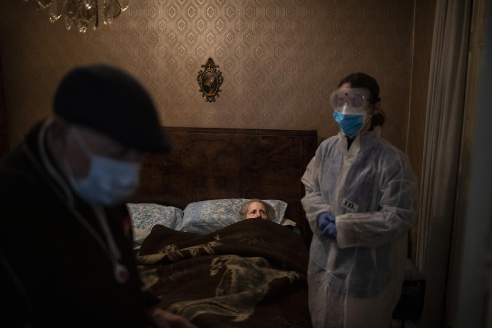 Josefa Ribas, 86, who is bedridden, looks at nurse Alba Rodriguez as Ribas' husband, Jose Marcos, 89, stands by in their home in Barcelona, Spain, March 30, 2020, during the coronavirus outbreak. Ribas suffers from dementia, and Marcos fears for them both if the virus enters their home. "If I get the virus, who will take care of my wife?" The image was part of a series by Associated Press photographer Emilio Morenatti that won the 2021 Pulitzer Prize for feature photography. (AP Photo/Emilio Morenatti)