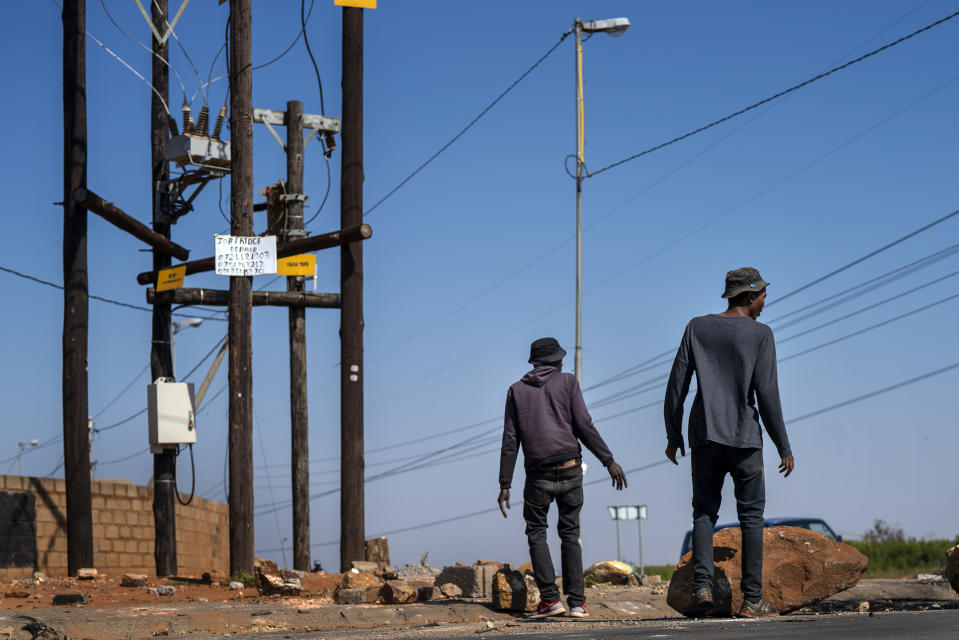 FILE- In this file photo taken Wednesday May 13, 2020, residents of the Snake Park neighborhood of Soweto outside Johannesburg, South Africa, walk through debris following a protest. South Africa is struggling to balance its fight against the coronavirus with its dire need to resume economic activity. The country with the Africa’s most developed economy also has its highest number of infections — more than 19,000. (AP Photo/Jerome Delay, File)