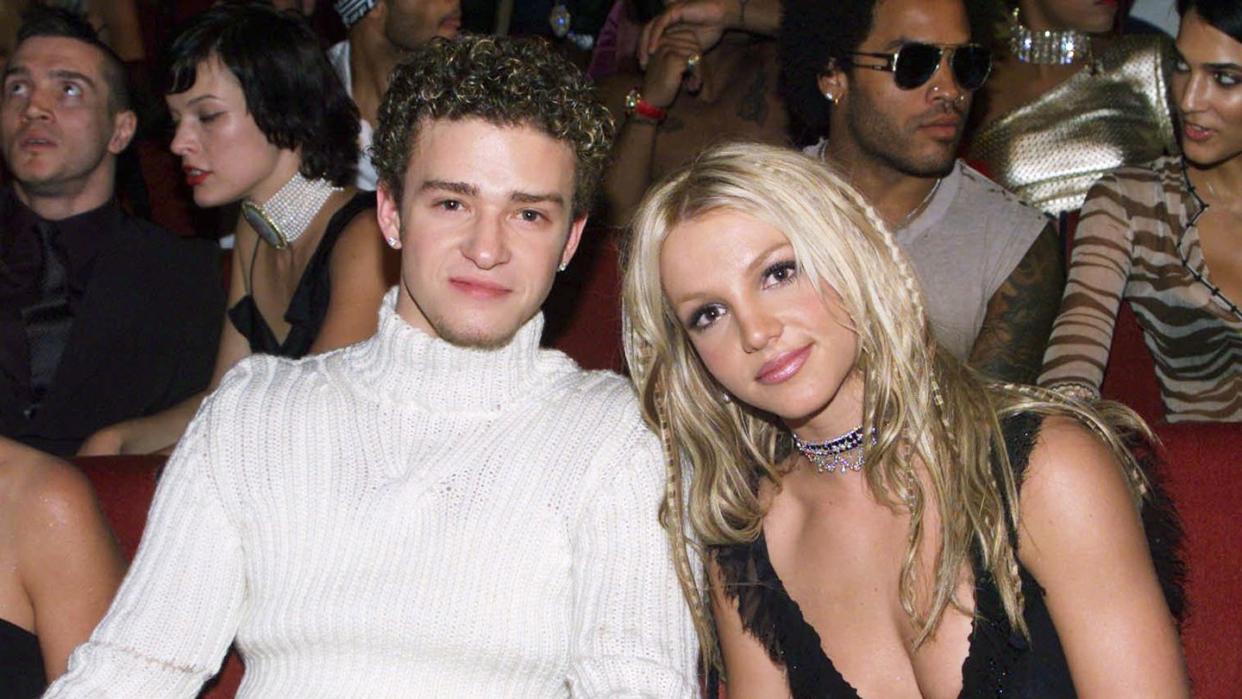 britney spears and justin timberlake in the audience at the 2000 mtv music video awards, with justin wearing a tight white turtleneck sweater and britney wearing a black camisole
