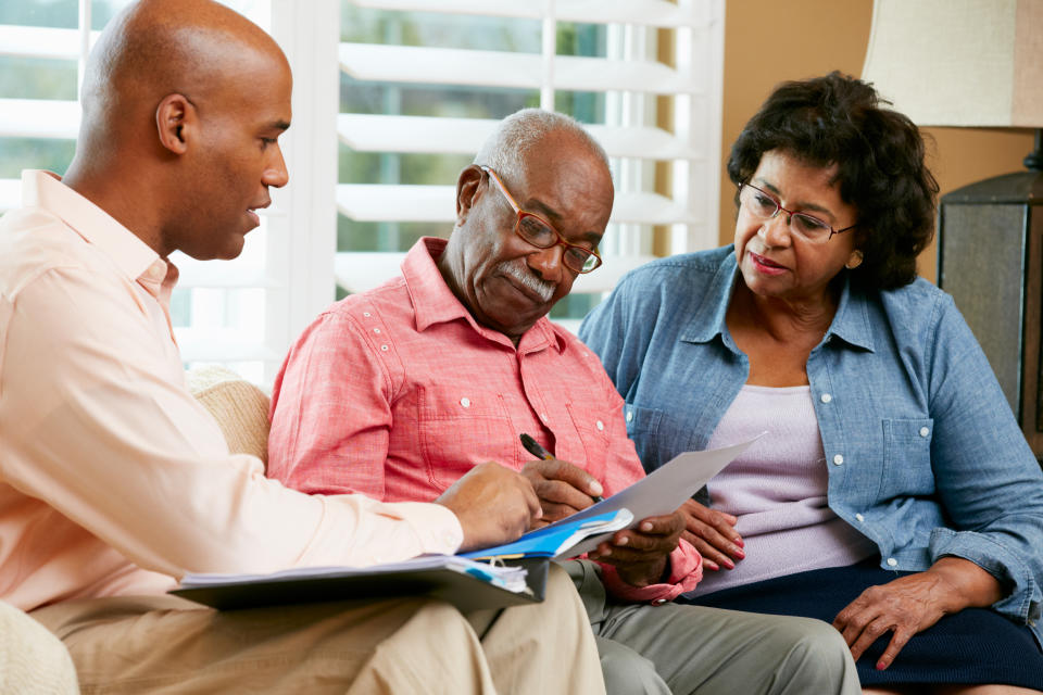 Financial Advisor Talking To Senior Couple At Home Signing Documents Sitting On Sofa