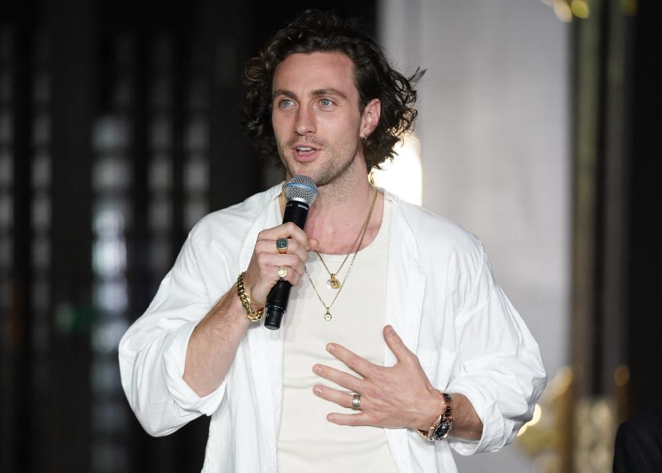 Aaron Taylor-Johnson in a white shirt holding a microphone