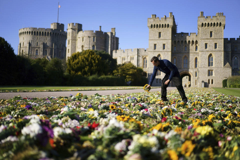 Workers from the Crown Estate move the floral tributes laid by members of the public outside Windsor Castle onto Cambridge Drive, near the Long Walk, Windsor, Sunday Sept. 18, 2022 ahead of the funeral of Queen Elizabeth II on Monday. (Victoria Jones/PA via AP)