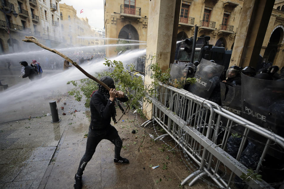 Anti-government demonstrators clash with riot police at a road leading to the parliament building in Beirut, Lebanon, Saturday, Jan. 18, 2020. Riot police fired tears gas and sprayed protesters with water cannons near parliament building to disperse thousands of people after riots broke out during a march against the ruling elite amid a severe economic crisis. (AP Photo/Hassan Ammar)