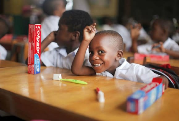 Smiling child with toothbrush and Crest toothpaste on table in a room with other children.