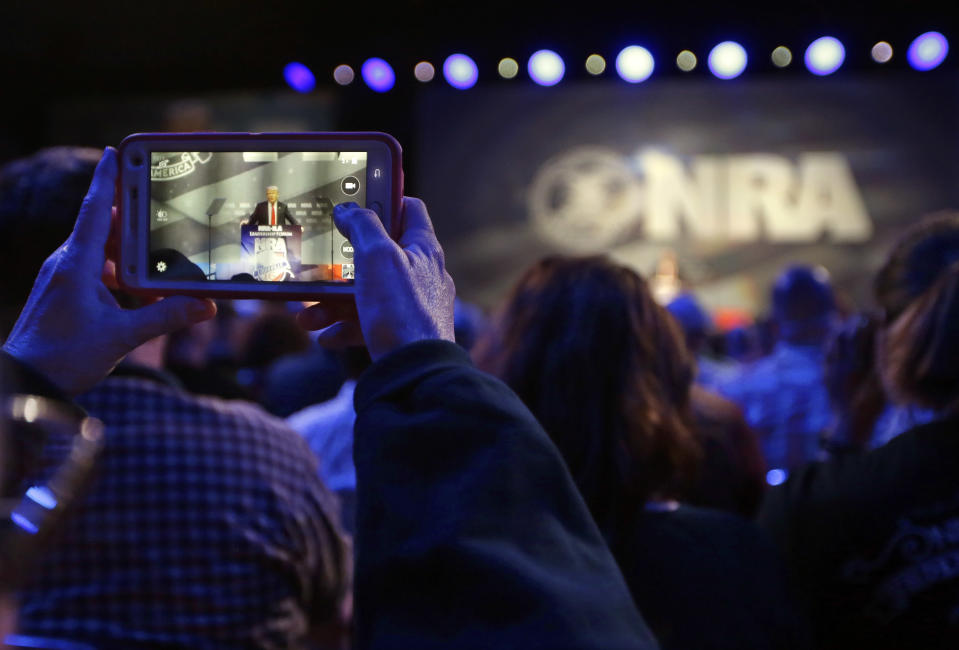 FILE - In this May 20, 2016, file photo, a National Rifle Association attendee photographs Republican presidential candidate Donald Trump as he speaks at the NRA convention in Louisville, Ky. The organization has been closely aligned with Trump, who will be addressing the 2019 NRA annual meeting, the third consecutive year he’s appeared before the group. (AP Photo/Mark Humphrey, File)