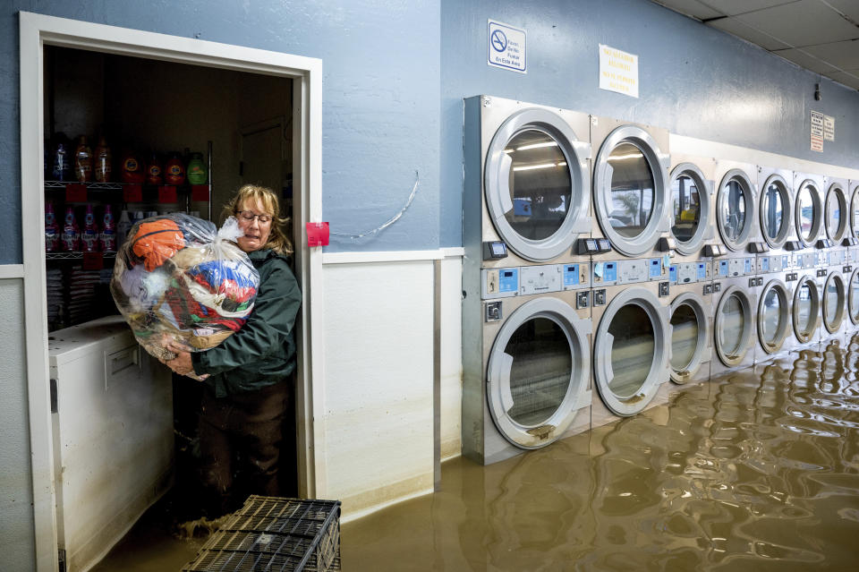 Pamela Cerruti carries clothing from Pajaro Coin Laundry as floodwaters surround machines in the community of Pajaro in Monterey County, Calif., on Tuesday, March 14, 2023. "We lost it all. That's half a million dollars of equipment," said Pamela who added that they plan to rebuild. (AP Photo/Noah Berger)